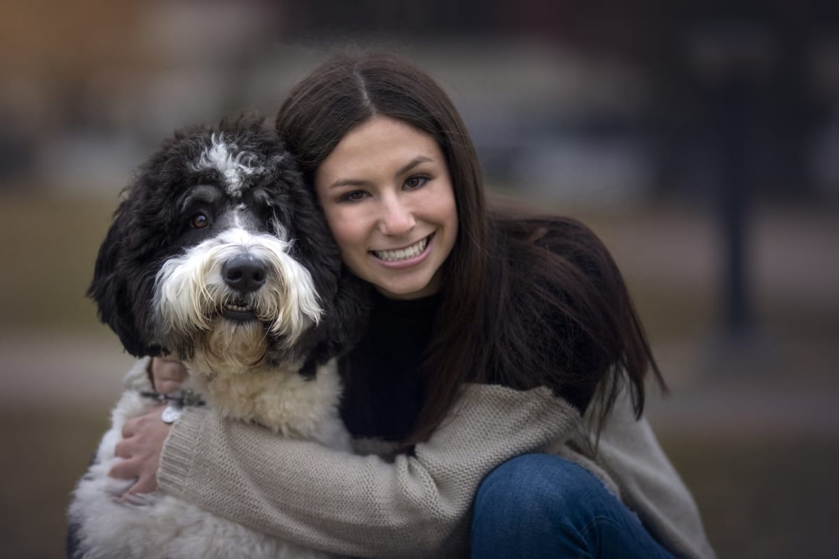 Girl smiles while holding her dog as part of a high school senior photoshoot in Detroit
