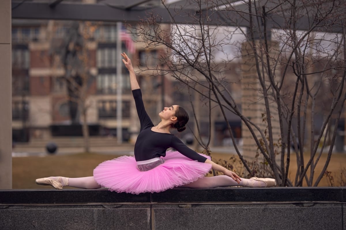 Dancer, wearing a pink tutu and black top, strikes a beautiful pose in the splits, beautifully photographed by a skilled Detroit dance photographer.