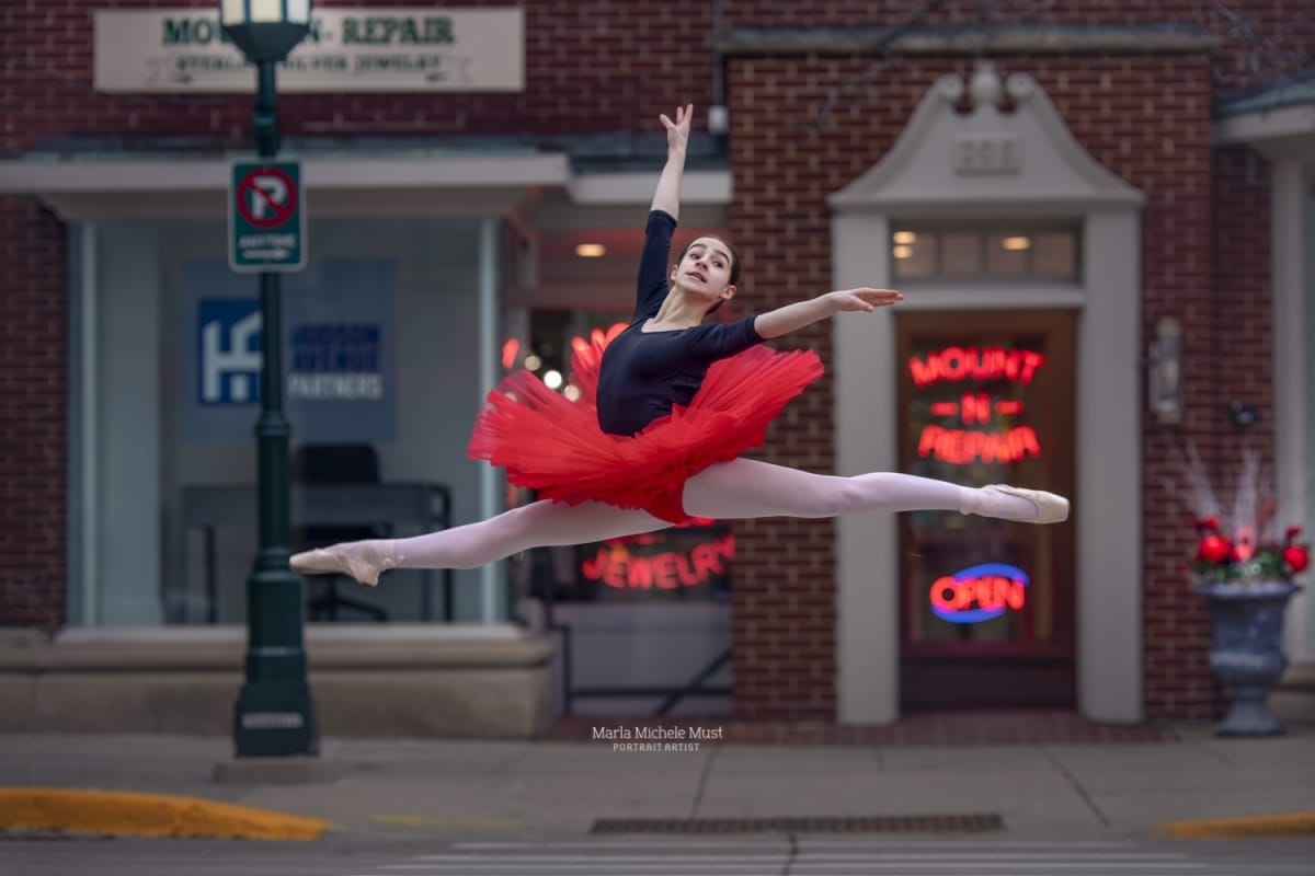 Artistry and precision are displayed as a ballerina soars into the air wearing a red tutu, skillfully photographed during a dance photoshoot by a Detroit-based photographer.