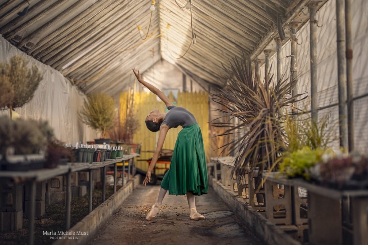 A dancer's lyrical pose radiates emotion and beauty in an upward stretch while wearing a bright green skirt, beautifully photographed in a greenhouse by a skilled Detroit dance photographer