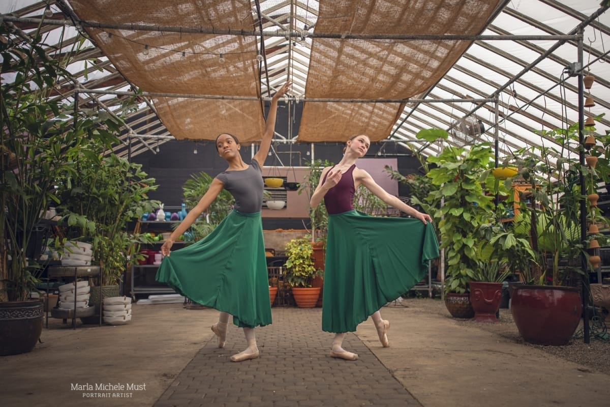 Two dancers mirror each other in a standing position in a greenhouse, captured by a Detroit-based photographer during a dance photoshoot.