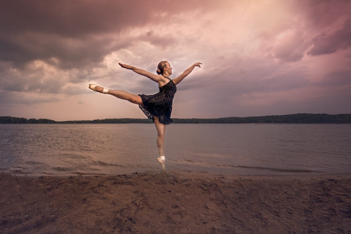 A Detroit dancer captures the essence of grace in a stunning leap during a dance photoshoot on a Michigan beach at sunset.