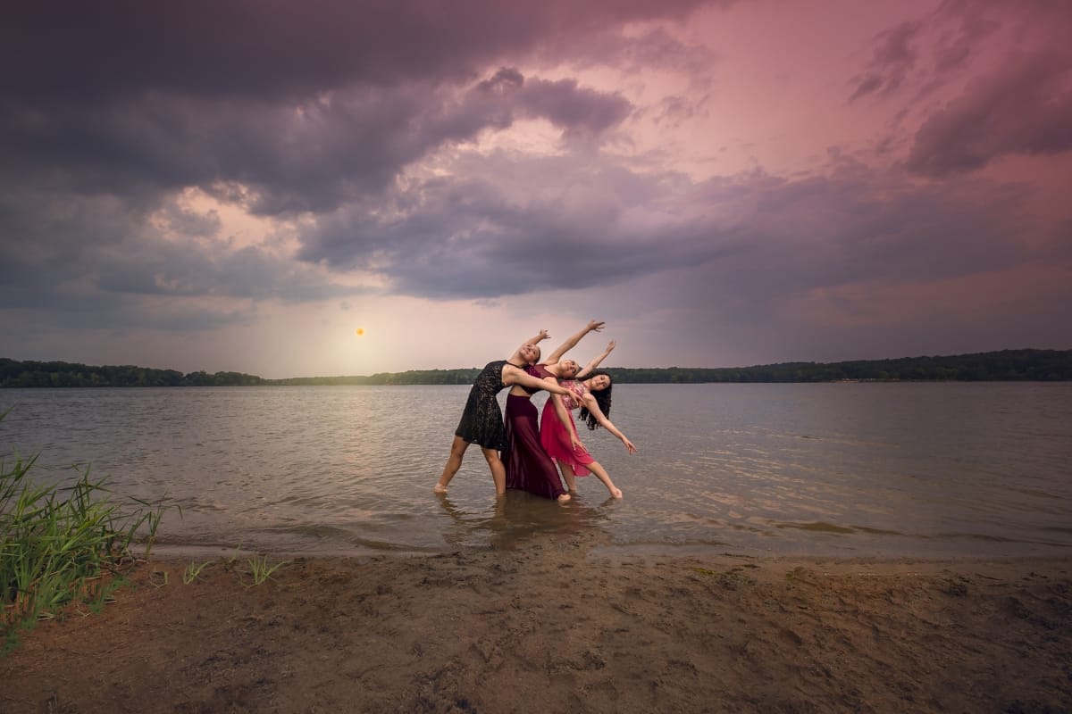 Three Detroit dancers emit a graceful essence in a contemporary pose as they lean against each other during a dance photoshoot on a Michigan beach at sunset.