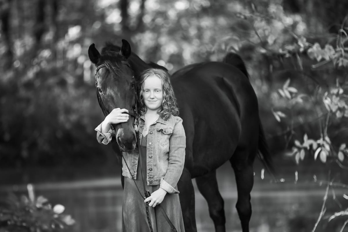 Black and white photo captured by a Detroit equine photographer, showcasing the bond between a horse and its owner, the owner holding her horse's nose gently against her chest. .
