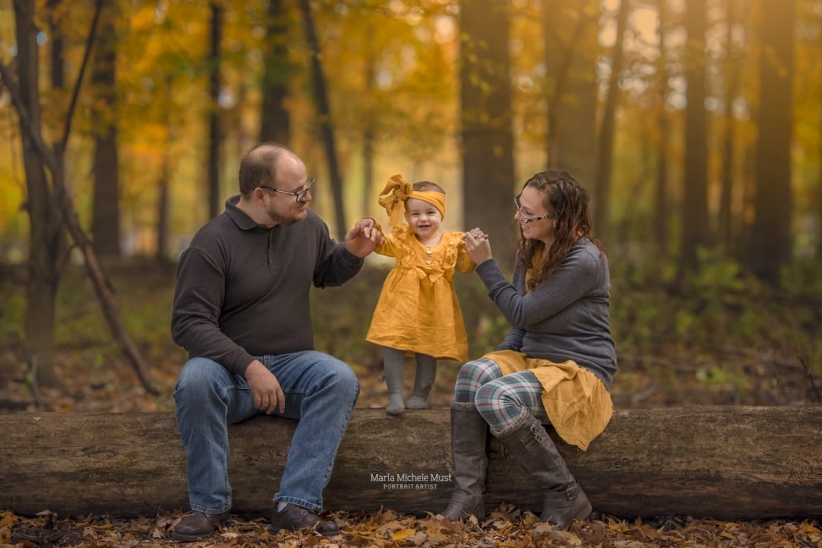 A local couple sits on a log in the forest, their child standing between them in a yellow rain jacket in the forests of Michigan.