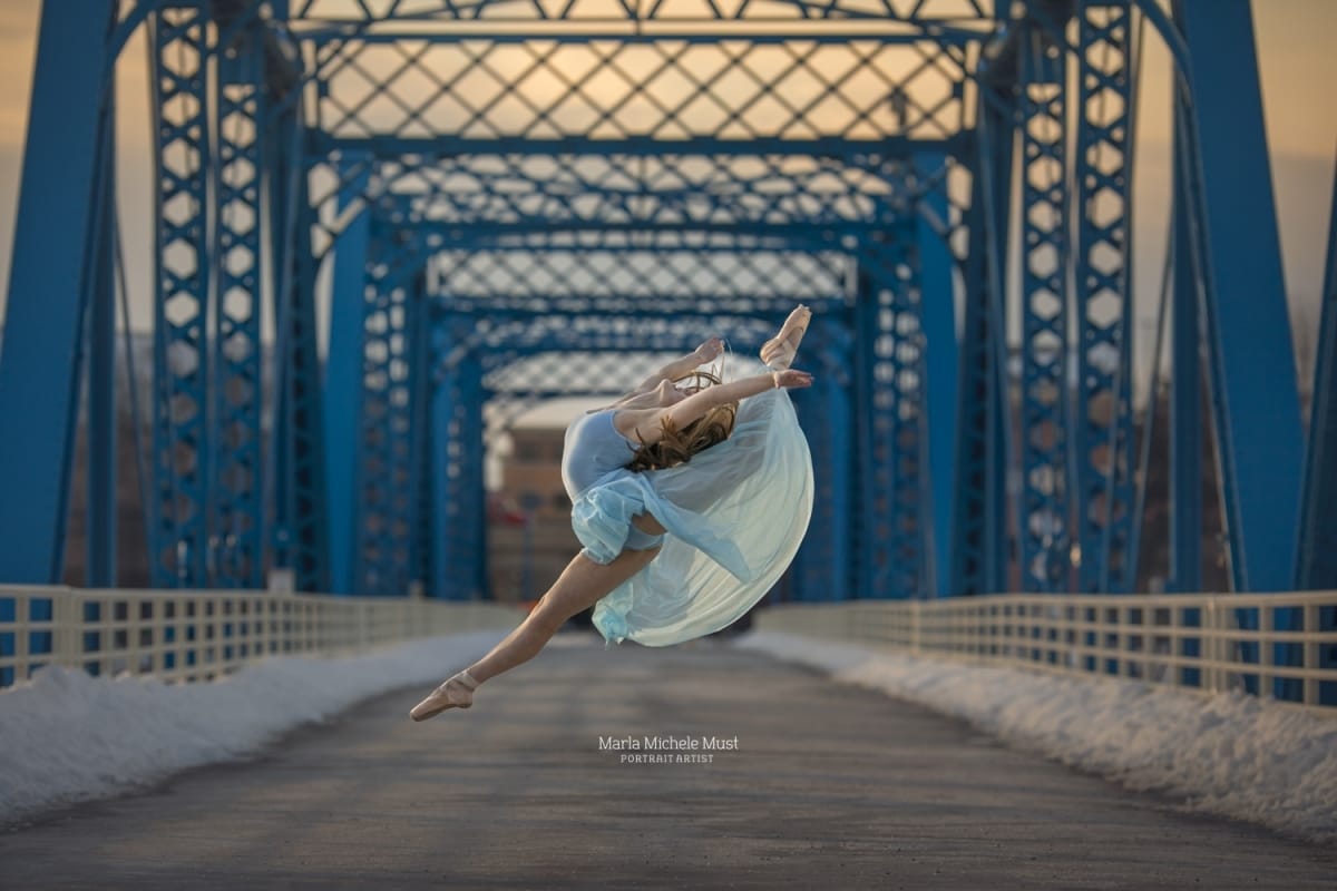 A dancer soars in the air during a photoshoot with a talented Detroit photographer, embodying the spirit of dance in a firebird leap upon a bridge.