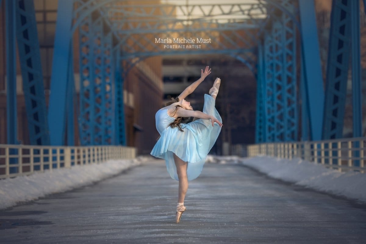 Dancer's leg and arm extensions through her light blue dress shine in this stunning dance portrait, captured by a talented Detroit photographer against a city bridge background.
