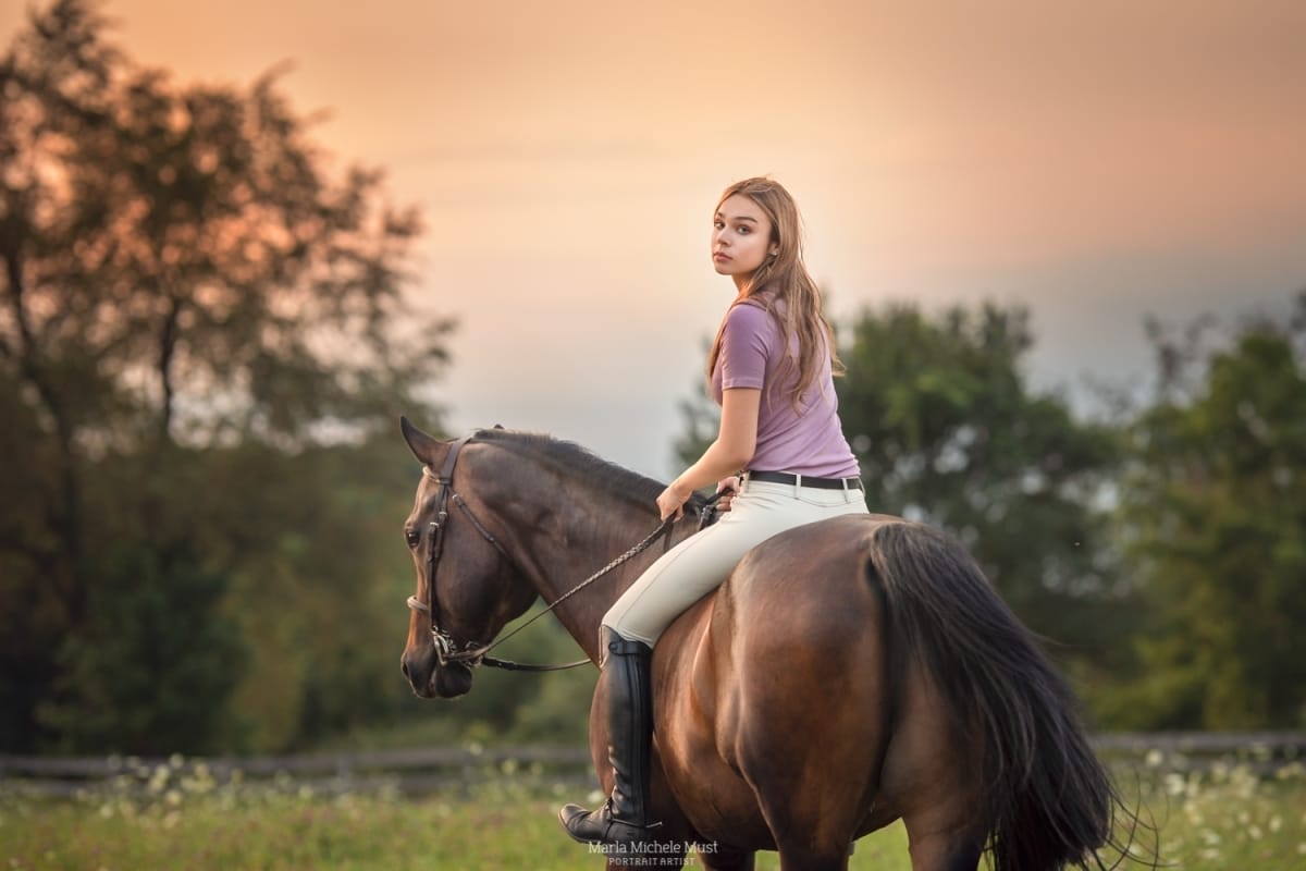 In the enchanting light of a sunset, a Detroit equine photographer captures a young horse and rider, the woman looking over her shoulder to the camera.