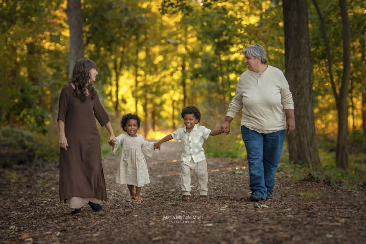 Local Detroit photographer captures family portrait of a couple walking through the forest with their children, holding hands.