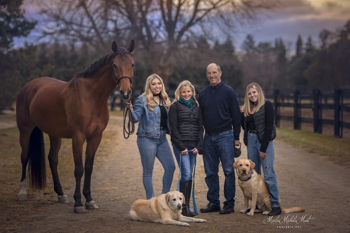 An autumnal moment captured by a Detroit equine photographer, highlighting the bond between a horse, their owner, family, and golden retriever against the backdrop of a trail.