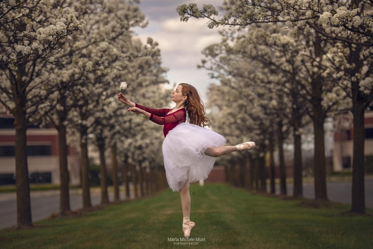 Impeccable technique showcased in a stunning portrait of a dancer in mid-air, taken by a talented Detroit photographer among a grove of evenly spaced cherry trees.