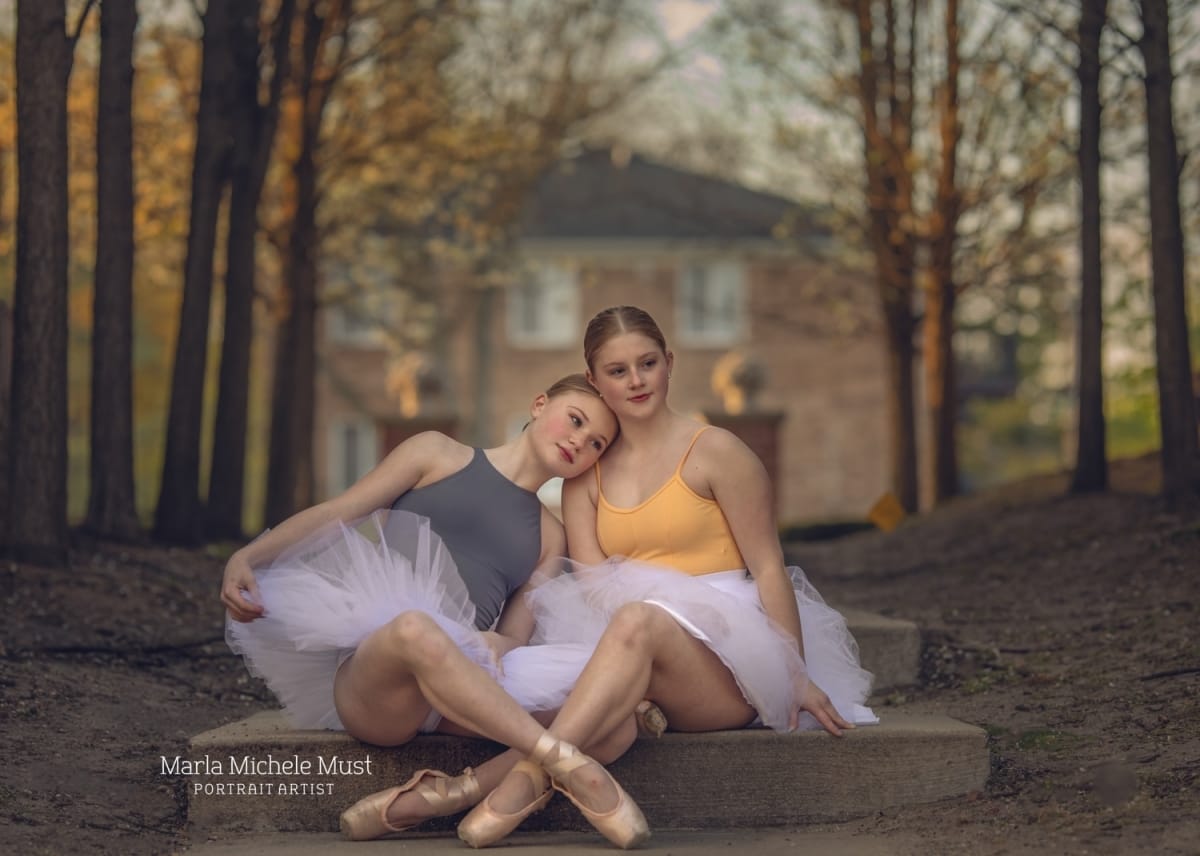 Two ballerinas sit in tutus and pointe shoes on stone steps during a Detroit-based dance portraits.
