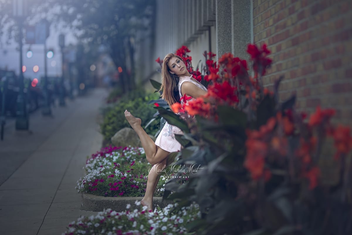 Dancer's effortless pose with one leg in the air while gracefully leaning towards vibrant flowerbeds shines in this captivating photo from a Detroit dance photoshoot.