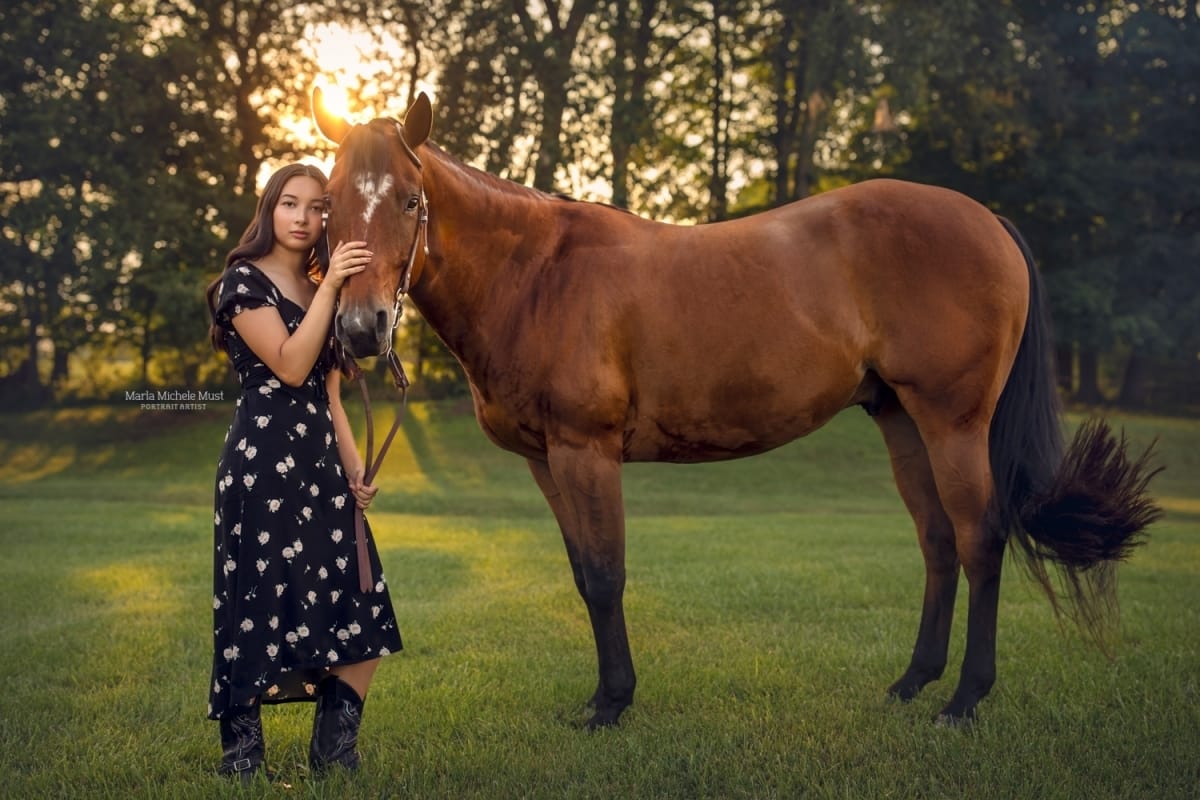 A Detroit horse and rider portrait: Horse owner gently grasping the horse's nose against a summer sunset and grassy field.