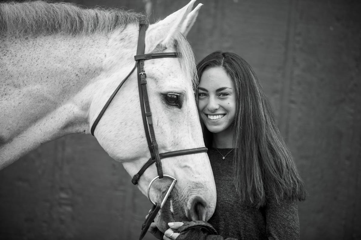 Black and white horse owner portrait for a Detroit equine photographer: Embracing the horse's nose with care and smiles happily at the camera.