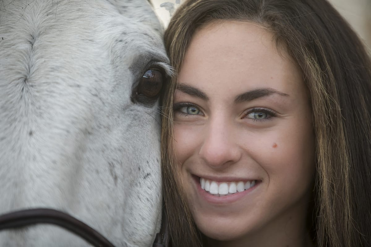 Detroit equine photographer's capture: Horse owner's intimate connection captured in a close-up portrait of a woman and her horse as she smiles to the camera, only the horse's eye and muzzle in view.