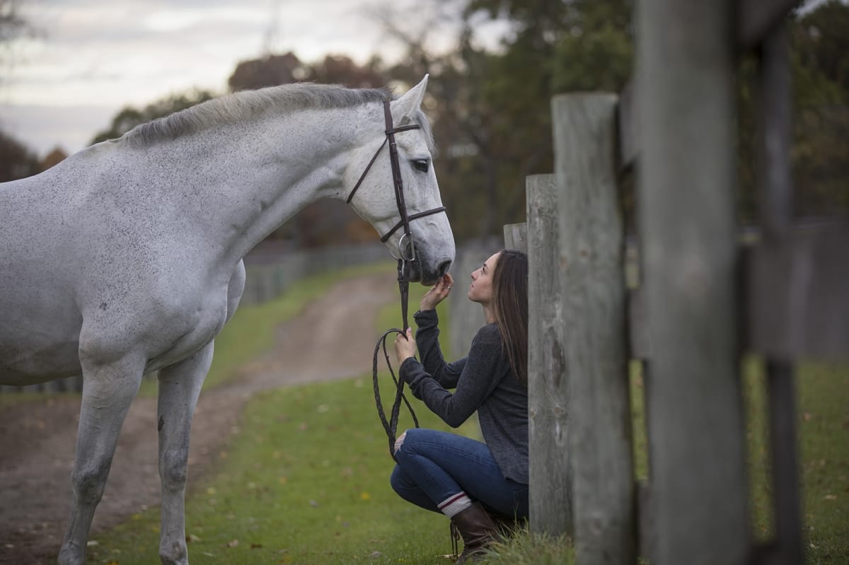 Trailside photograph by a Detroit equine photographer, revealing the bond between a horse and its owner as she hold her horse's reins and nose gently above her.
