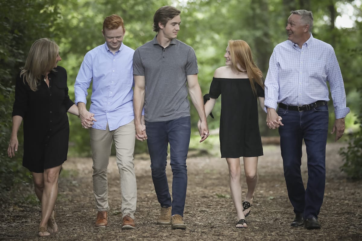 A family photo of three men and a woman hold hands while walking along a path outdoors.