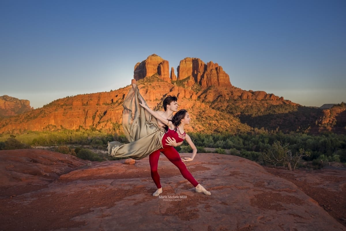 Dancer couple's lyrical pose shines in this captivating image from a dancer photoshoot with a talented Detroit photographer in a desert landscape, a rocky formation behind them.