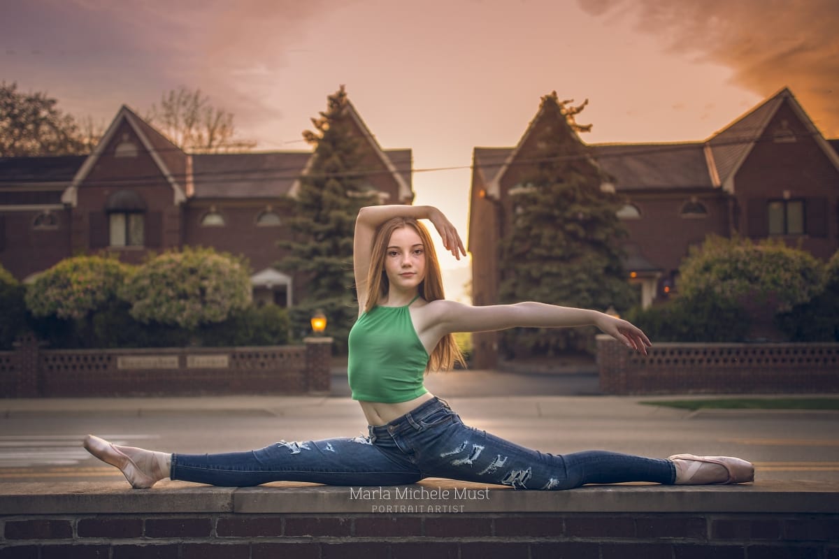 Dancer, wearing casual clothes, strikes a beautiful pose in the splits, beautifully photographed in in a quiet residential courtyardby a skilled Detroit dance photographer.