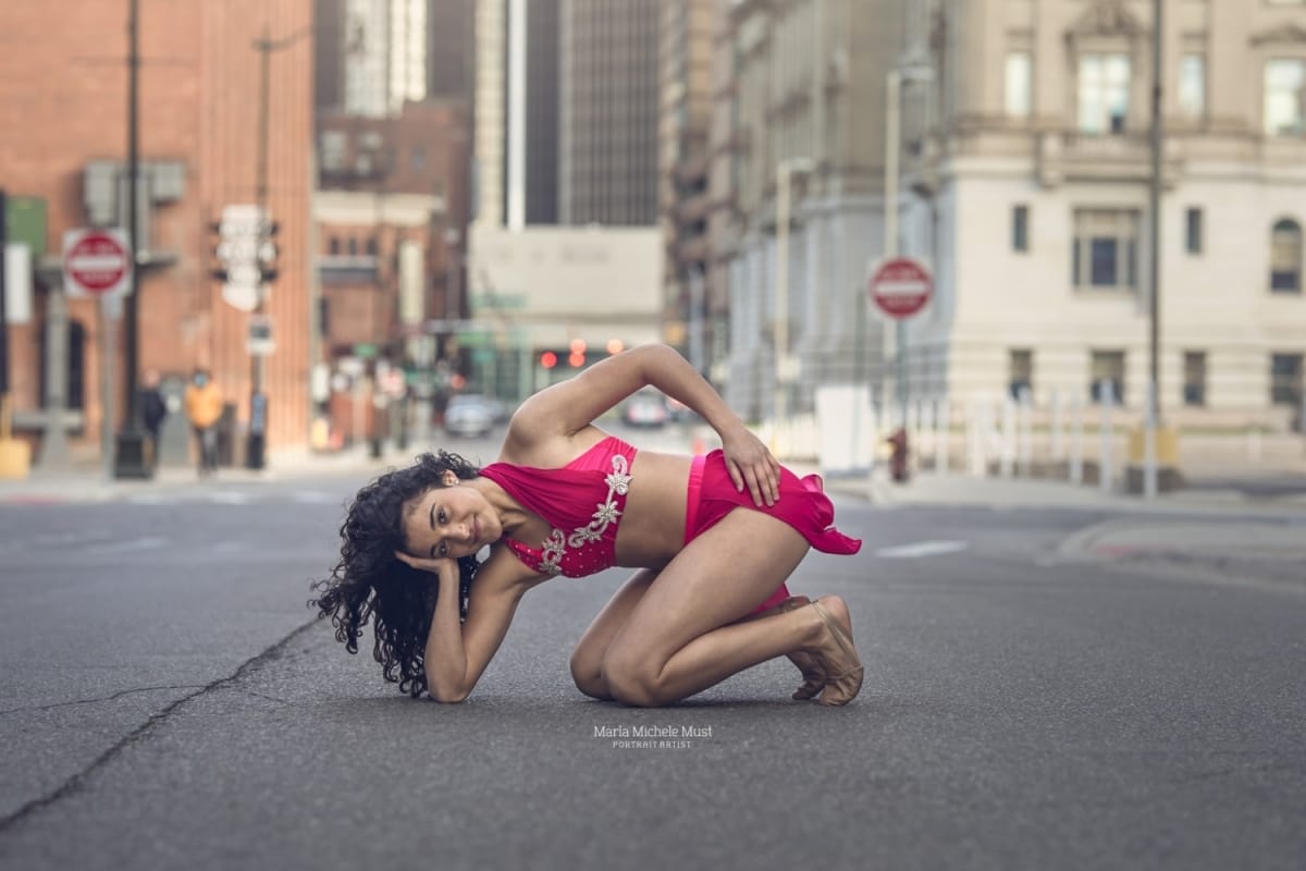 Detroit dancer poses resting her head in her hand, crouched over the Detroit street below during a dancer photoshoot.