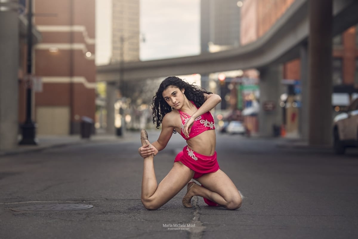 Detroit dancer poses kneeling on a Detroit street, reaching back to grab her ankle, during a dancer photoshoot.