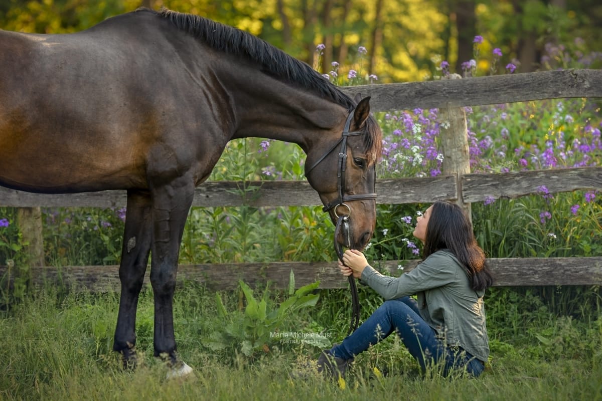 Woodland photograph by a Detroit equine photographer, revealing the bond between a horse and its owner as she hold her horse's reins and nose gently above her.