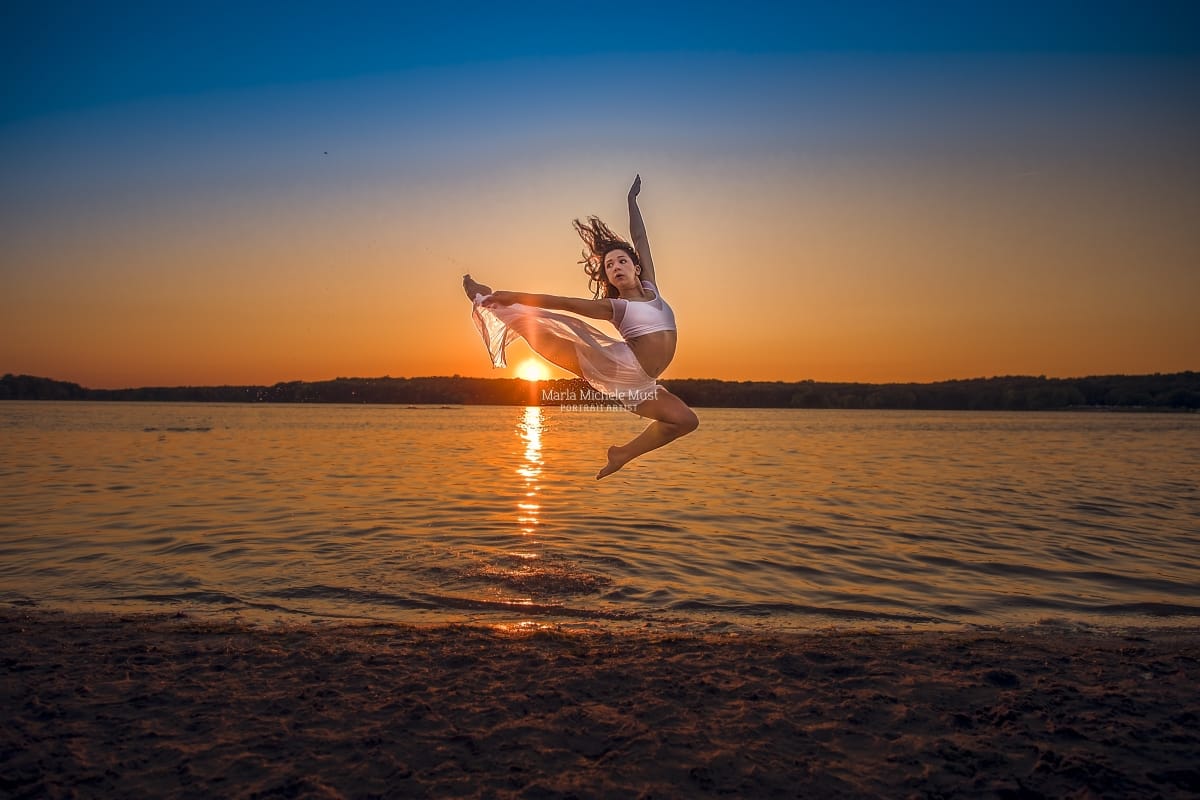 Detroit dancer captures the essence of grace in a stunning leap above water while holding white, flowing cloth during a dance photoshoot.