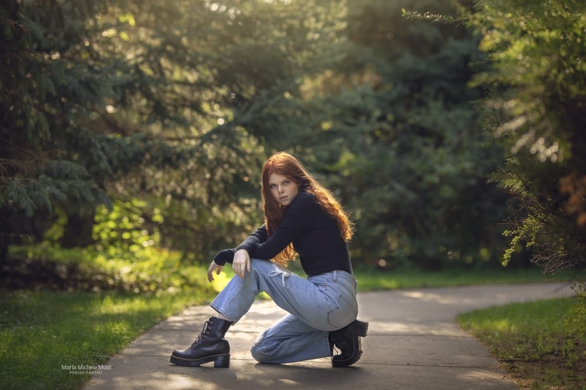 A Detroit high school senior girl poses knelt down on a path in a grunge-inspired pose for her senior portrait