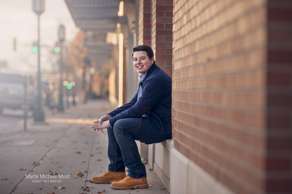 A high school senior portrait photoshoot captures the moment when a young man in formal wear sits on the ledge of a building in downtown Detroit