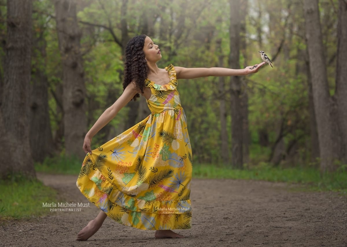 Dancer extends her arms outwards in profile while wearing a brightly colored dress on a Detroit trail during a dancer photoshoot.
