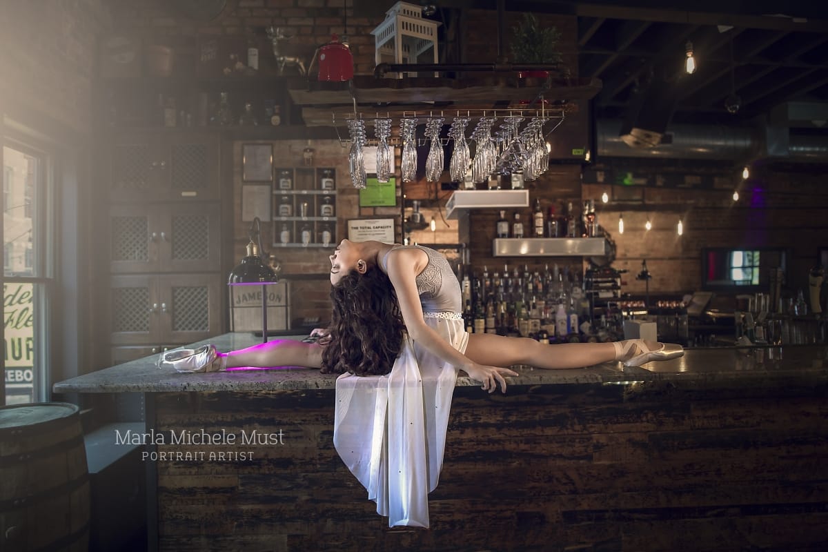 Elegantly dressed dancer fully tilts her head backwards in in the splits on a bar near Detroit, beautifully photographed by a skilled Detroit dance photographer.