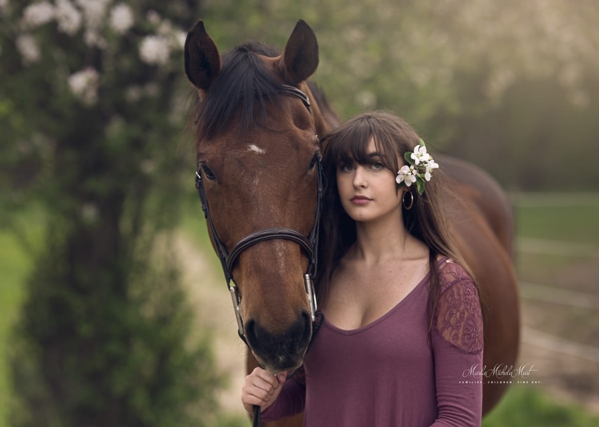Soulful portrait by a Detroit equine photographer, revealing the bond between a horse owner and their equine companion through a gentle grasp of the horse's reins, a flower in the owner's hair.