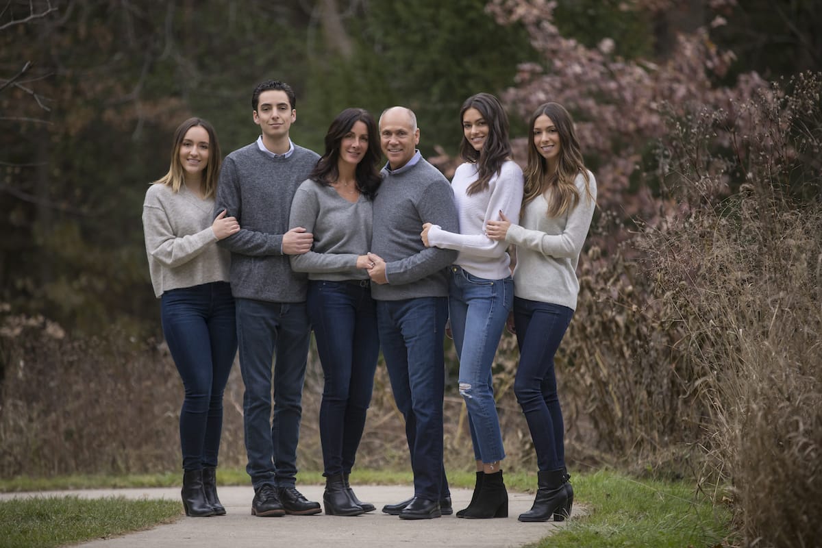 A group of young adults and their parents pose for a family portrait. They are all linking arms and wearing grey clothes.