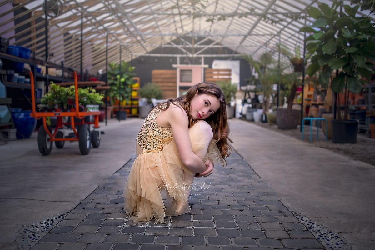 In a Detroit greenhouse, a dancer crouches while holding her knees during a Detroit dancer portrait photoshoot.