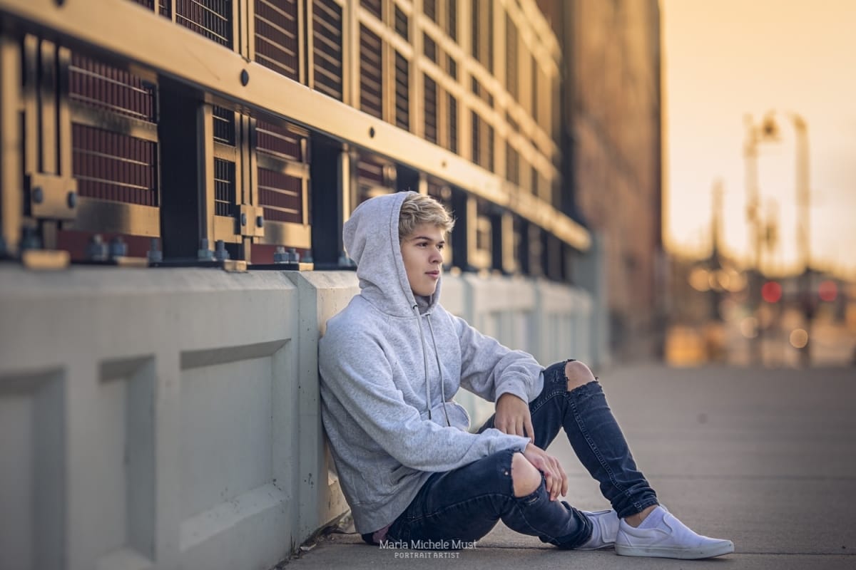 A high school senior portrait photoshoot captures the moment when a young man looks off camera while leaning against the wall of a downtown Detroit building