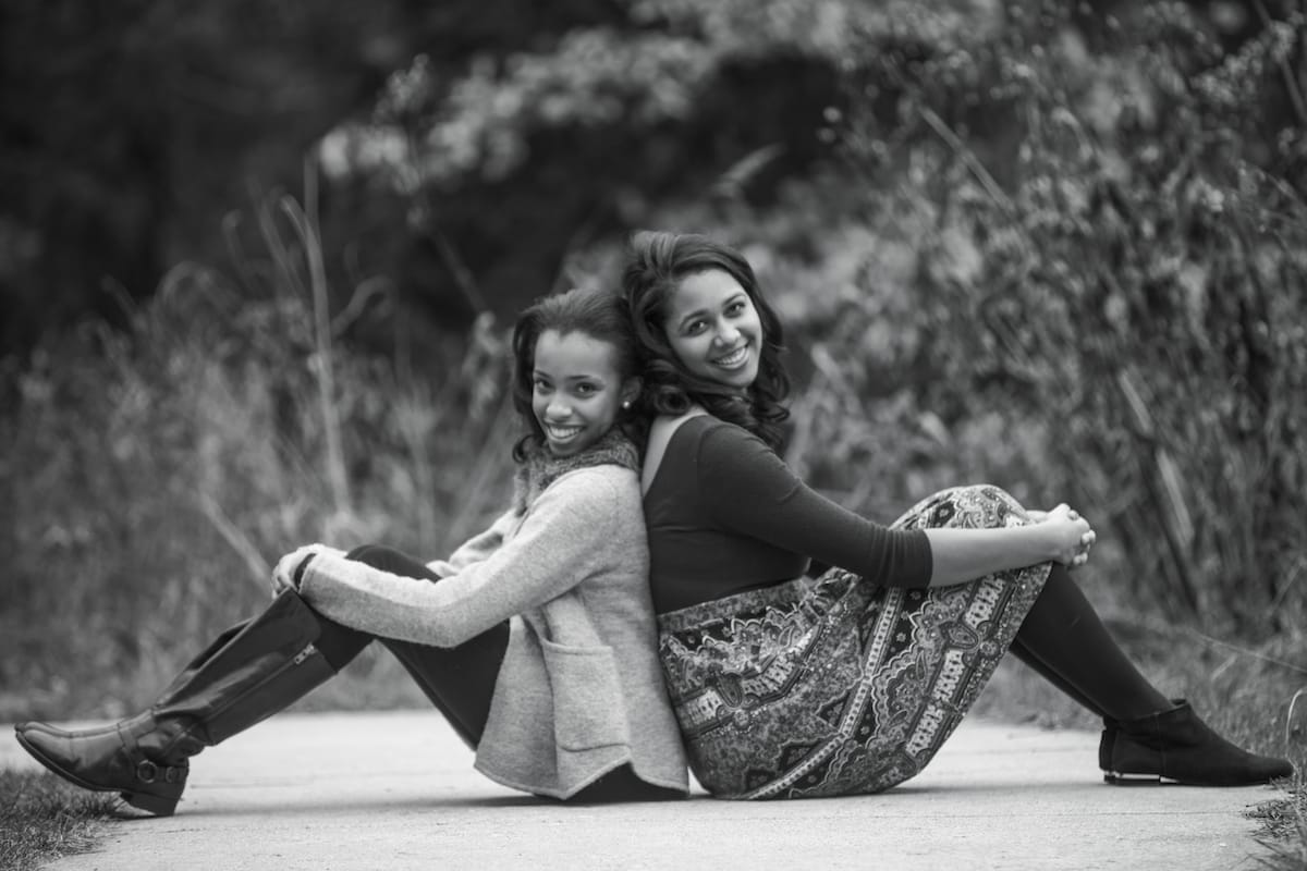A black and white photo of a mother and daughter sitting back to back and smiling with their eyes closed.