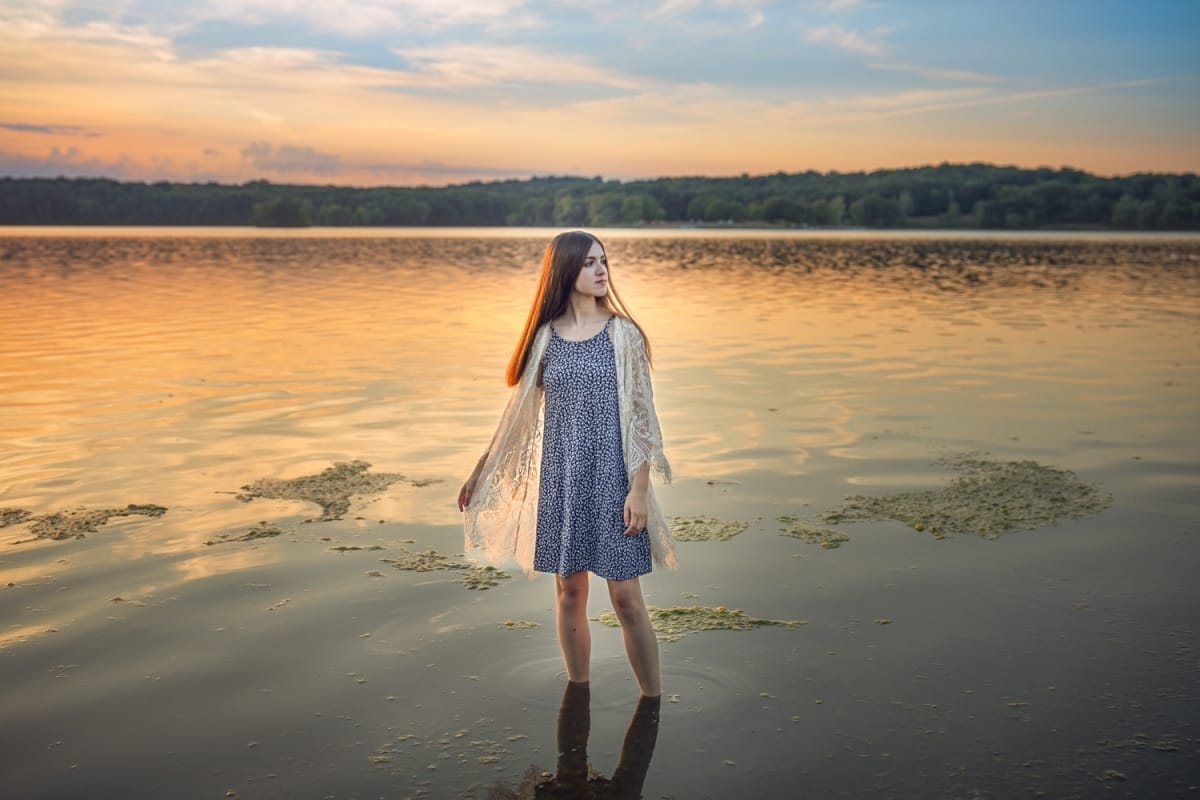Senior picture taken of a girl in a dress and cardigan looking over her shoulder as she walks along the beach of one of Michigan's great lakes