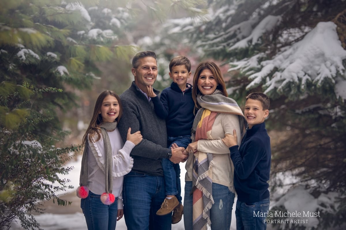 Local Detroit photographer winter family photoshoot idea. Family poses together in front of a snowy and green mountain.