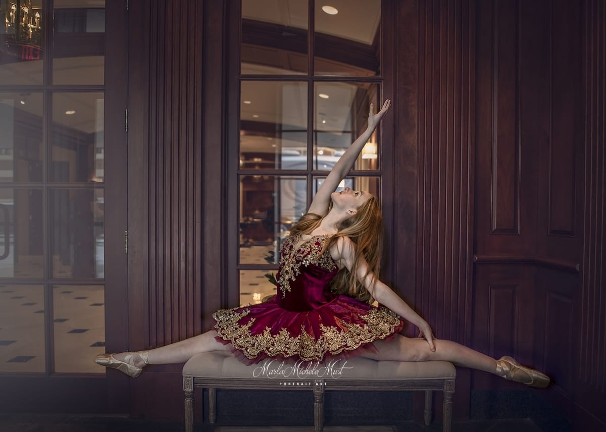 Posed in an early 20th century interior, a dancer does the splits in an intricately ornamented red and gold dress, her arm gracefully extended to the sky..