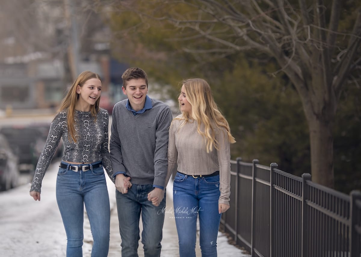 Three teen siblings walk along a bridge, laughing and talking with each other.
