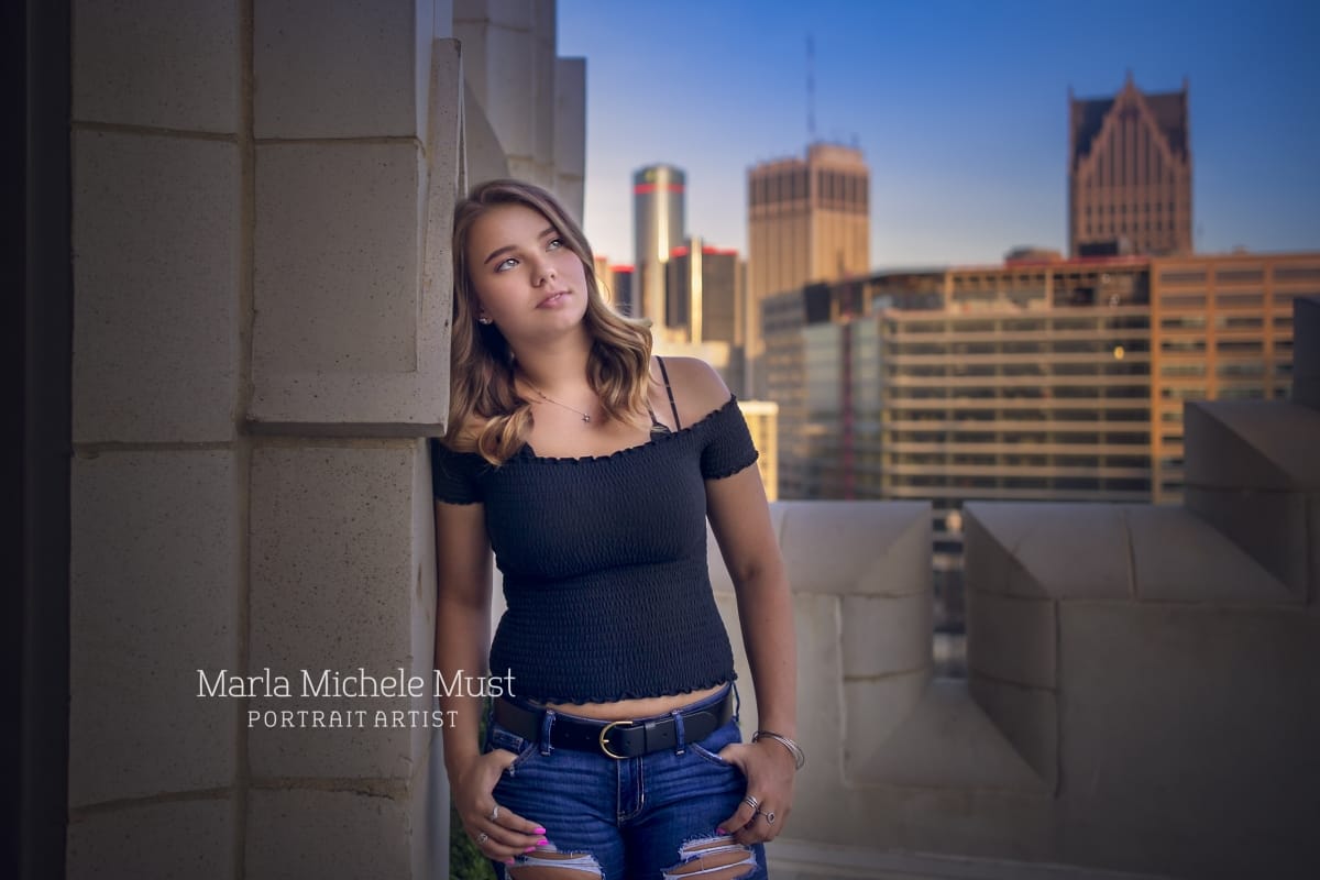 Senior picture taken of a girl looking thoughtfully into the distance, the skyline of a Michigan city behind her