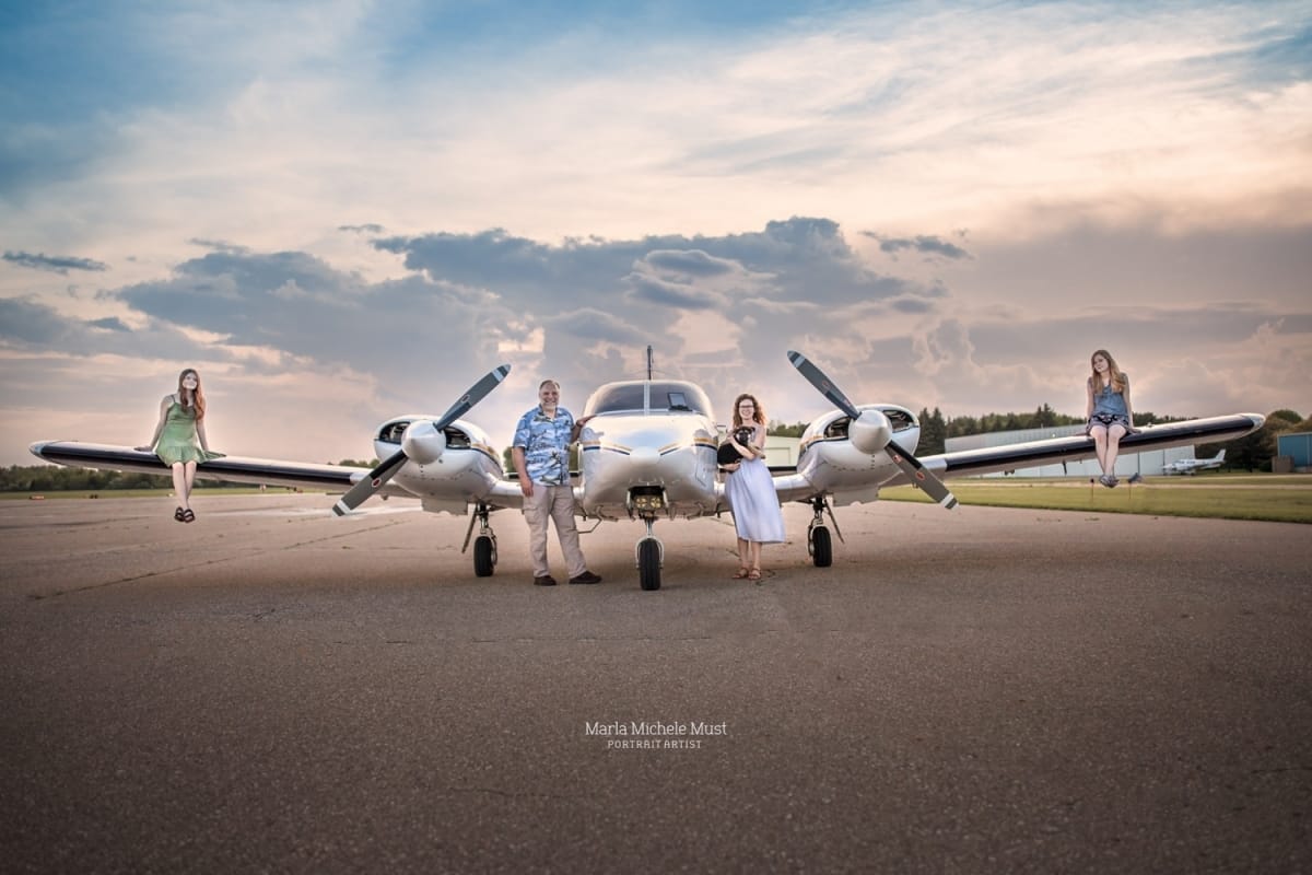 couple poses for a local family photographer while standing on either side of a small commercial airplane