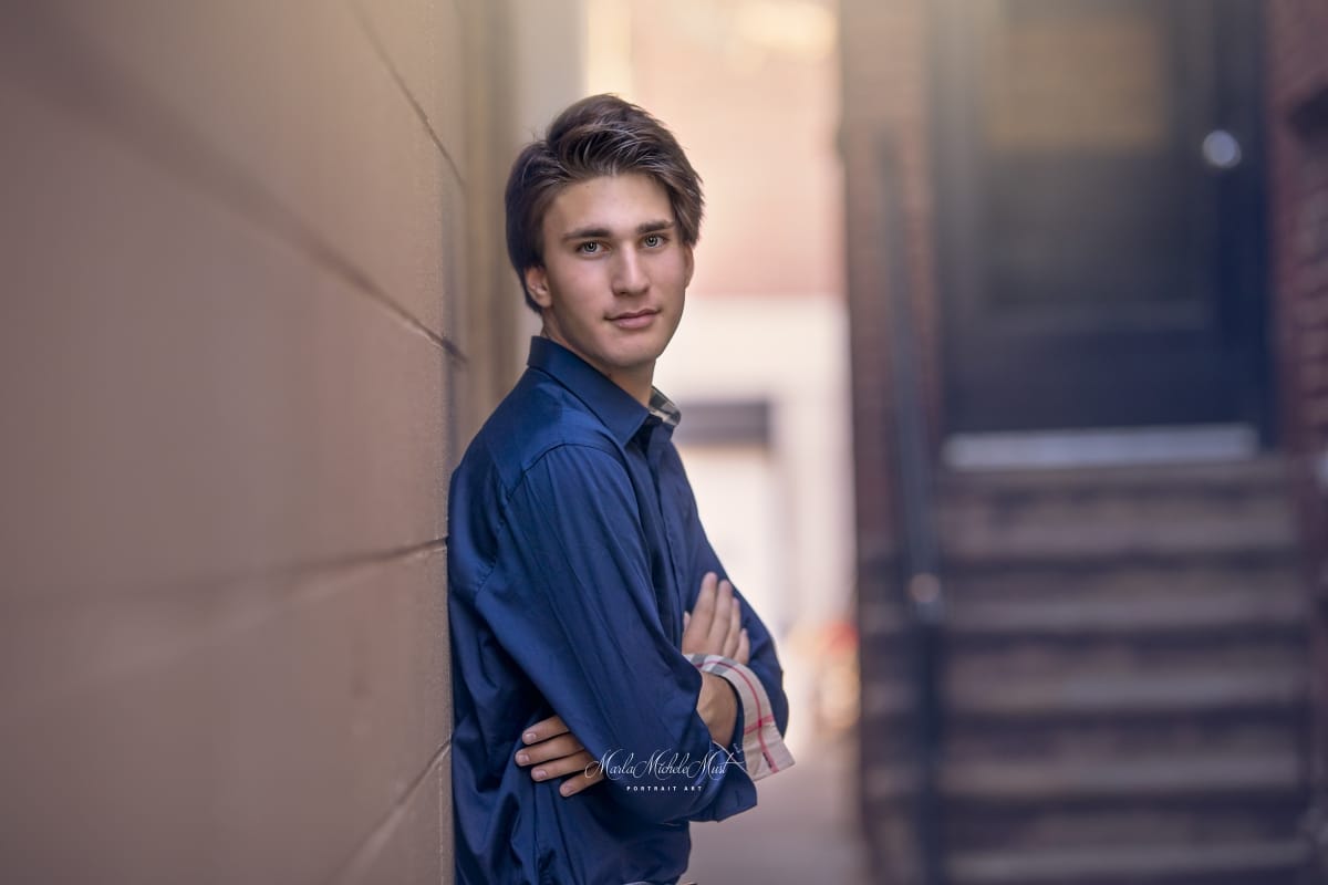 Detroit-area High school senior photo of a young man in formal wear with arms crossed leaning with his back against a wall looking at the camera