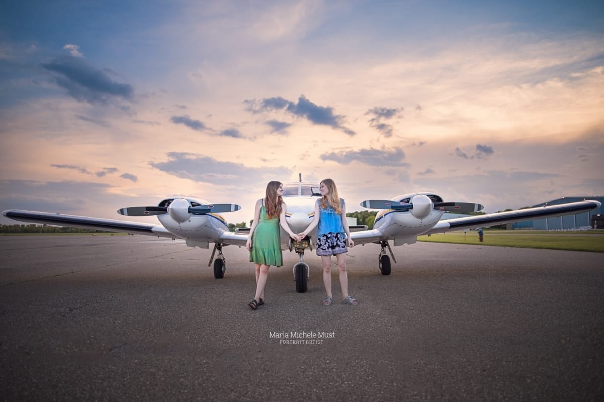 A couple pose for a local family photographer while standing on either side of a small commercial airplane.