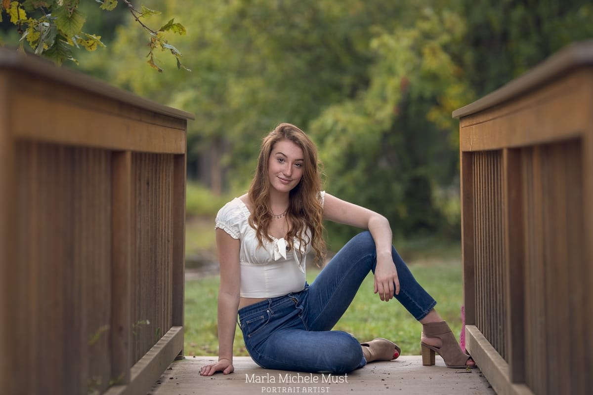 high school senior portrait of a girl sitting on a Detroit park bridge while resting her arm on her knee