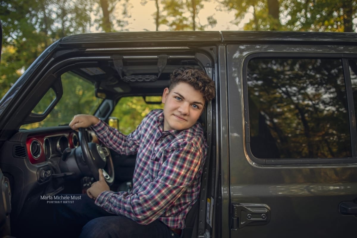 Detroit-area High school senior picture photographer captures a graduation photo of a young man as he leans out of the driver's side of a truck and smiles