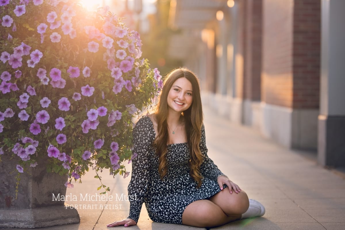 Detroit-area High school senior picture photographer captures a graduation photo of a girl sitting by a vase filled with flowers in a downtown Detroit shopping district