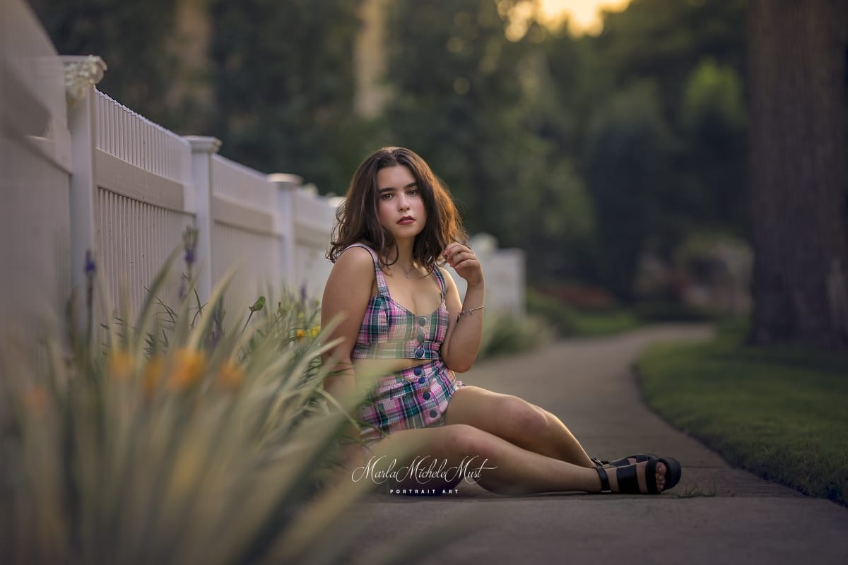 Detroit-area High school senior picture photographer captures a graduation photo of a girl sitting on the pathway of a nearby park surrounded by flowers