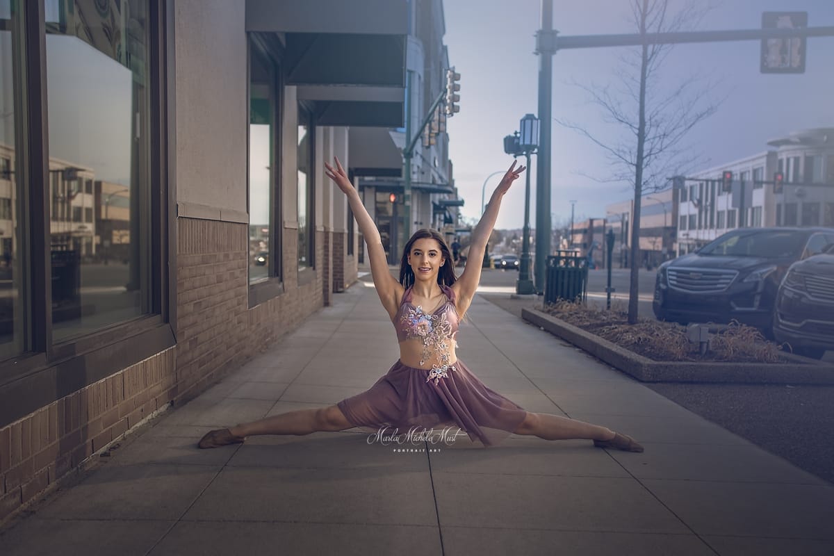 Posed on a Detroit sidewalk, a dancer does the splits in a flowing skirt and fitting top in neutral tones, her arm gracefully extended to the sky..